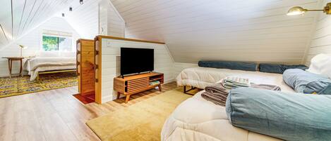 A cozy attic bedroom with a loft bed, a flat-screen TV, and a wooden dresser.