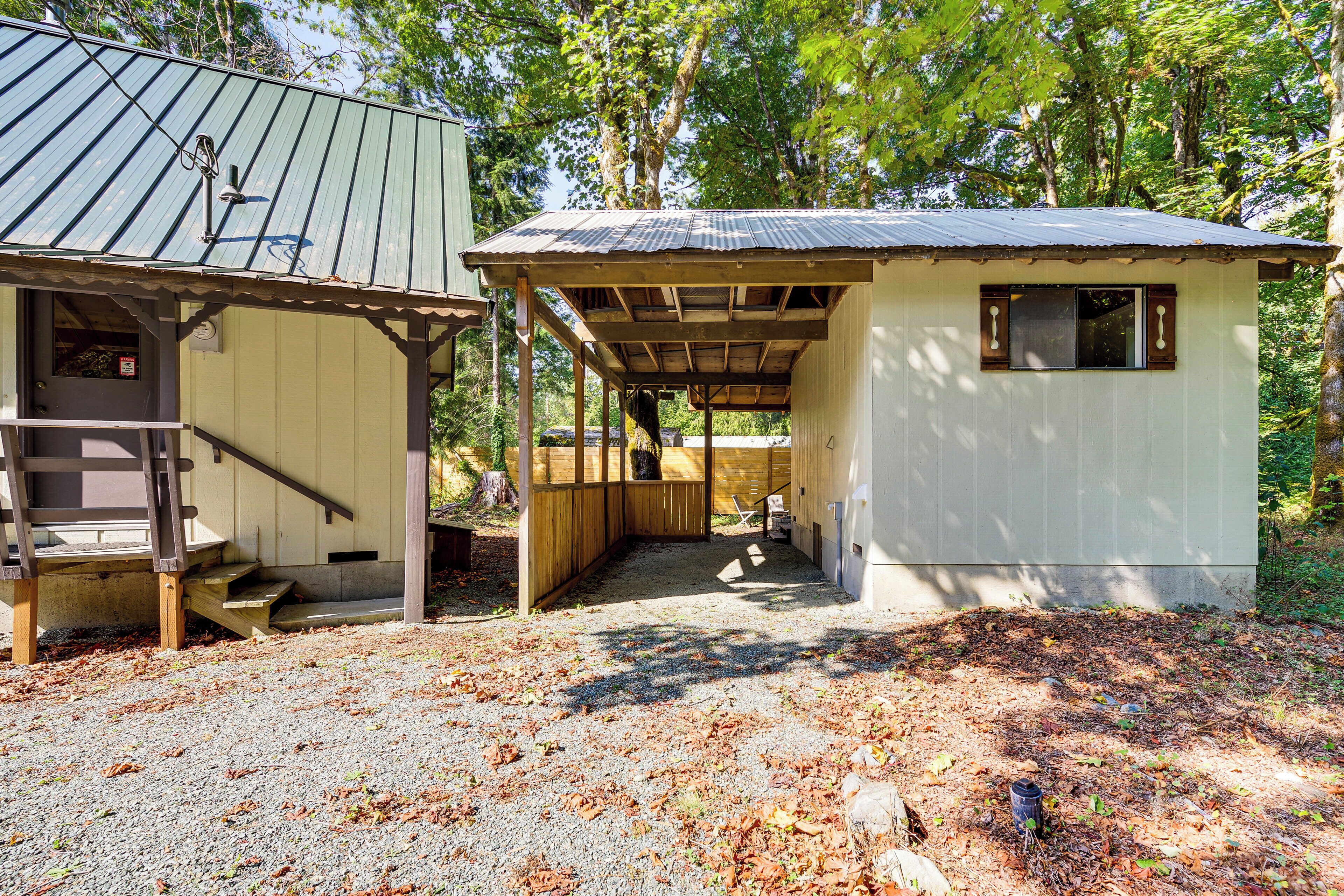 A rustic cabin with a wooden porch and a small attached shed, surrounded by trees.