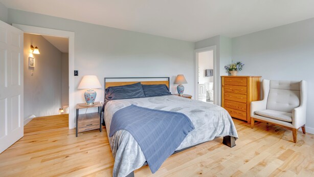 Un dormitorio con cama, lámparas de noche, cómoda, silla y puerta que da a otra habitación.
