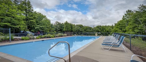 A swimming pool with a metal ladder, surrounded by a fence and trees.