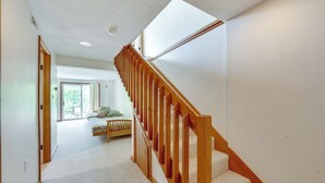 Un pasillo con una escalera de madera que conduce a un dormitorio con cama y ventana.