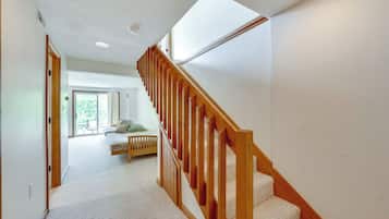 Un pasillo con una escalera de madera que conduce a un dormitorio con cama y ventana.