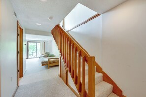 Un couloir avec un escalier en bois menant à une chambre à coucher équipée d’un lit et d’une fenêtre.