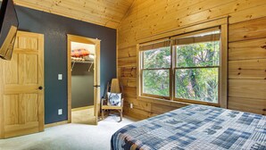 A bedroom with a bed, a window with a view of trees, a wooden door, and a chair with a pillow. - Ski & Hike: Mars Hill Mountaintop Cabin w/ Views (Mars Hill)