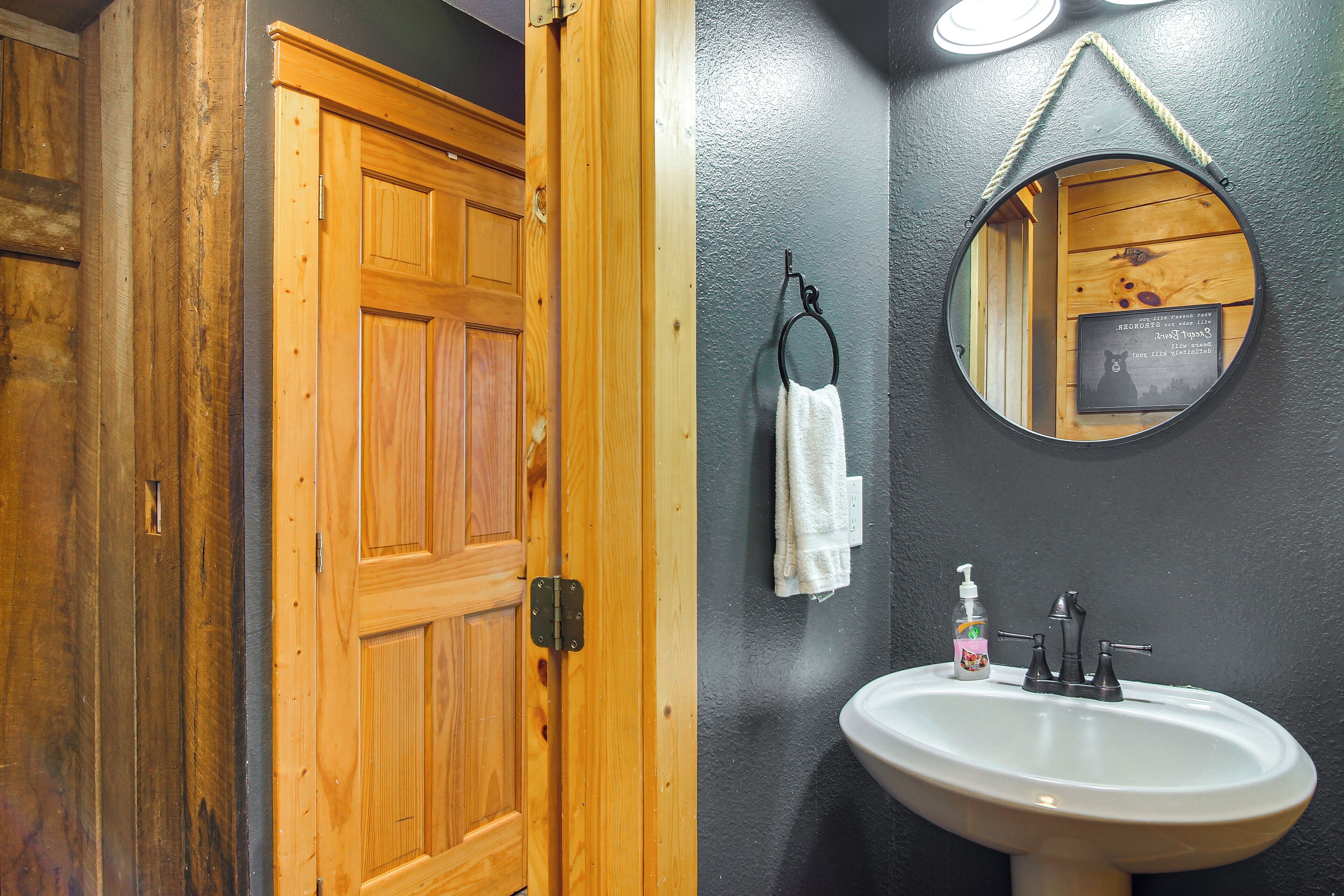 A bathroom with a wooden door, a sink with a mirror, and a towel hanging on a hook.