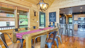 A wooden interior with a dining area featuring a long table and metal chairs, a kitchen with modern appliances, and a green door. - Ski & Hike: Mars Hill Mountaintop Cabin w/ Views (Mars Hill)