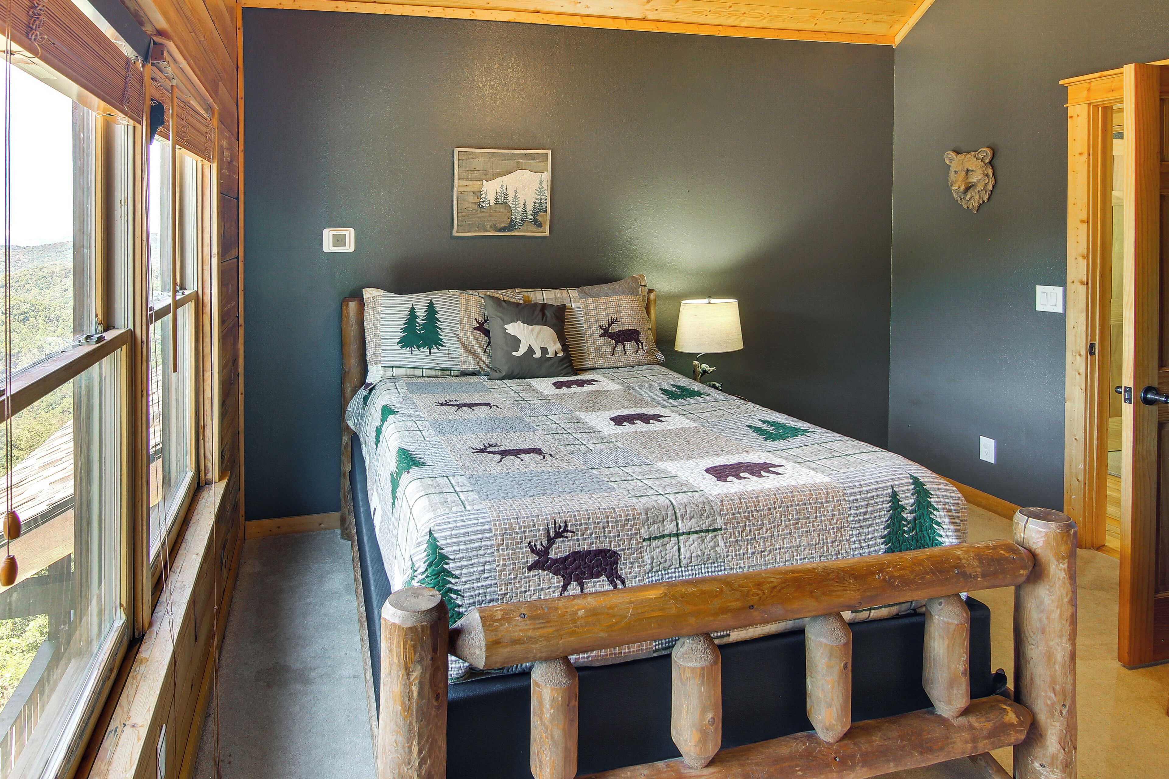Une chambre à coucher avec un lit, une tête de lit en bois, une fenêtre et une décoration représentant une tête d’ours au mur.