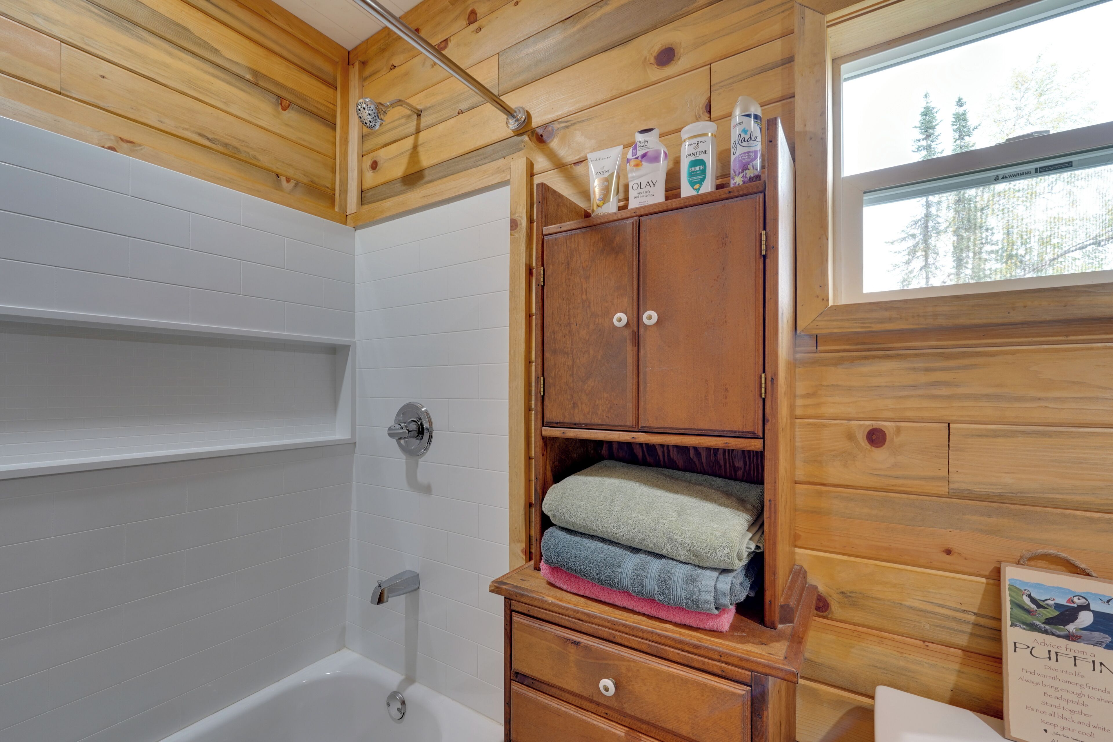 Ein Badezimmer einer Holzhütte mit einer Badewanne, Holzschränken und einem Fenster.