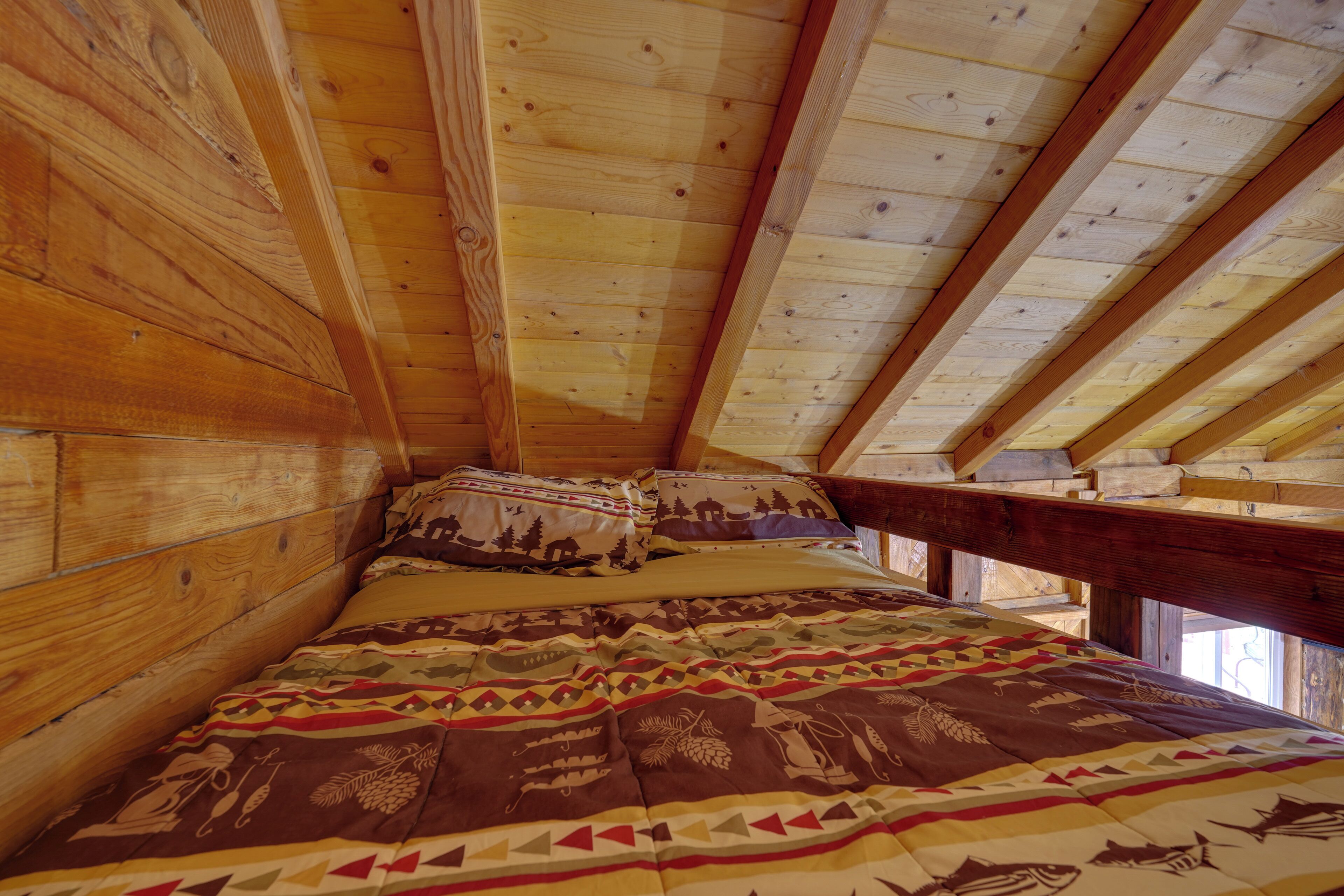 A wooden cabin room with a bed, pillows, and a window.