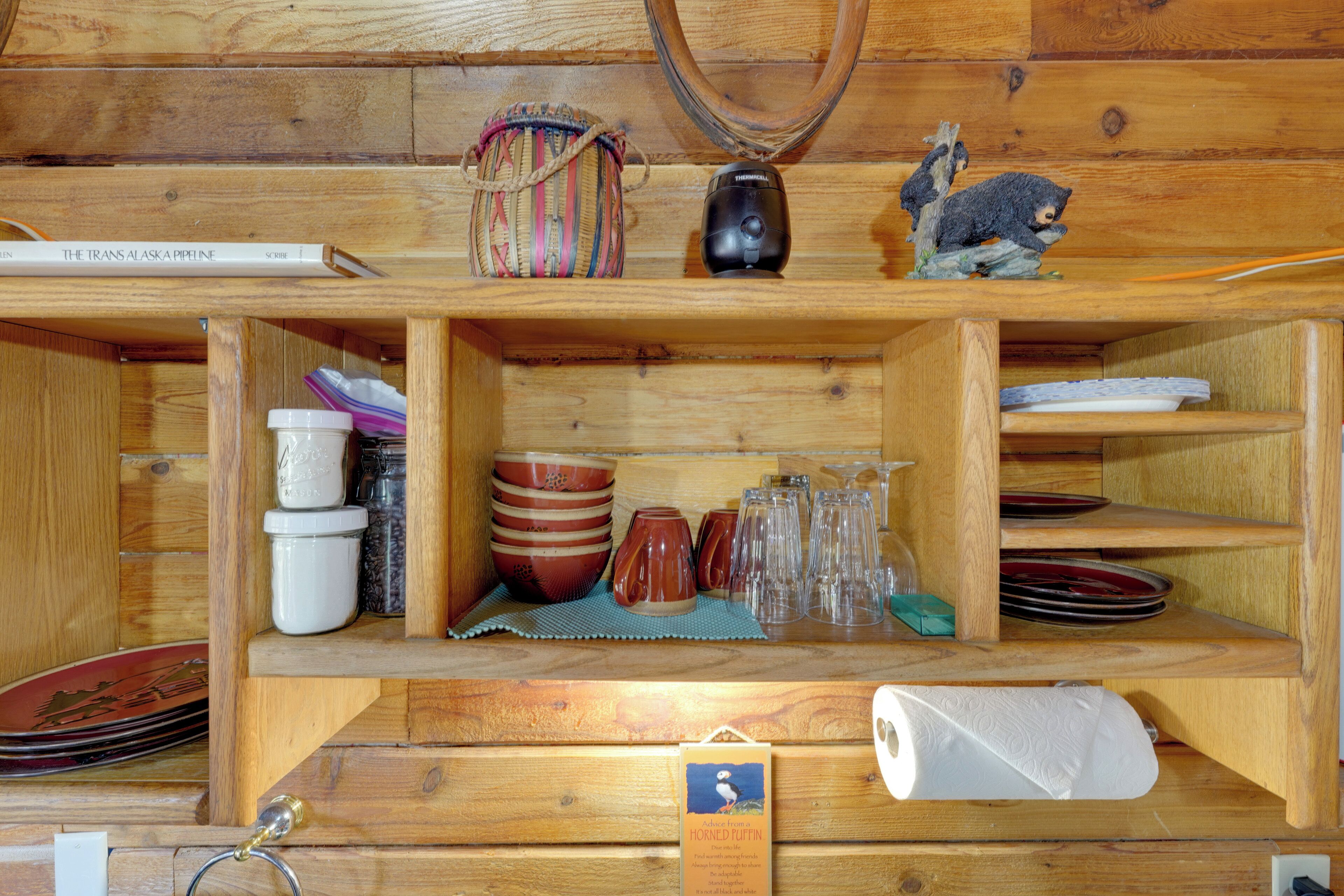 A wooden shelf with various items including a thermos, a small figurine, and a book titled 'The Trans Alaska Pipeline.'