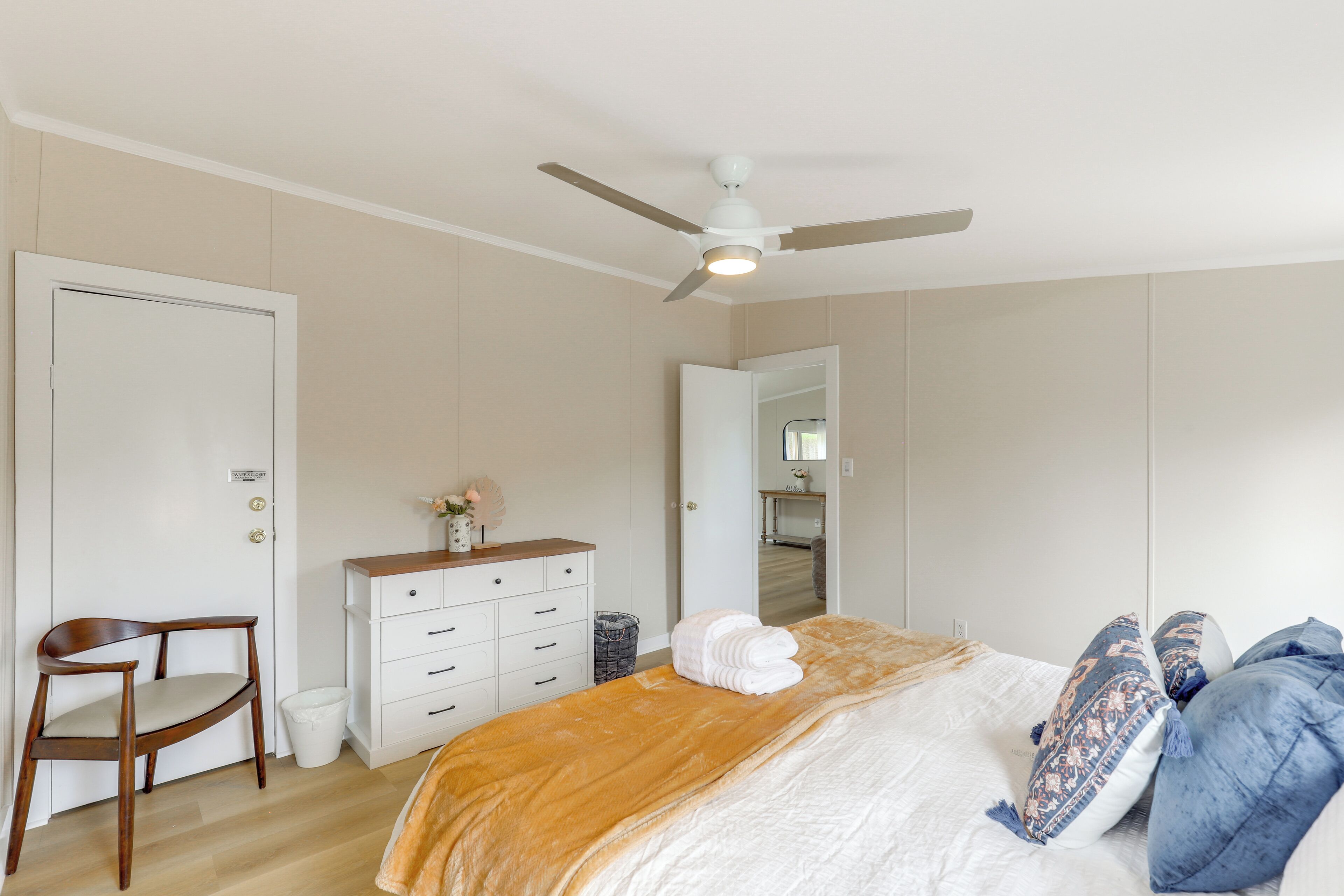 Ein Schlafzimmer mit Bett, Deckenventilator, Kommode, Stuhl und Tür.