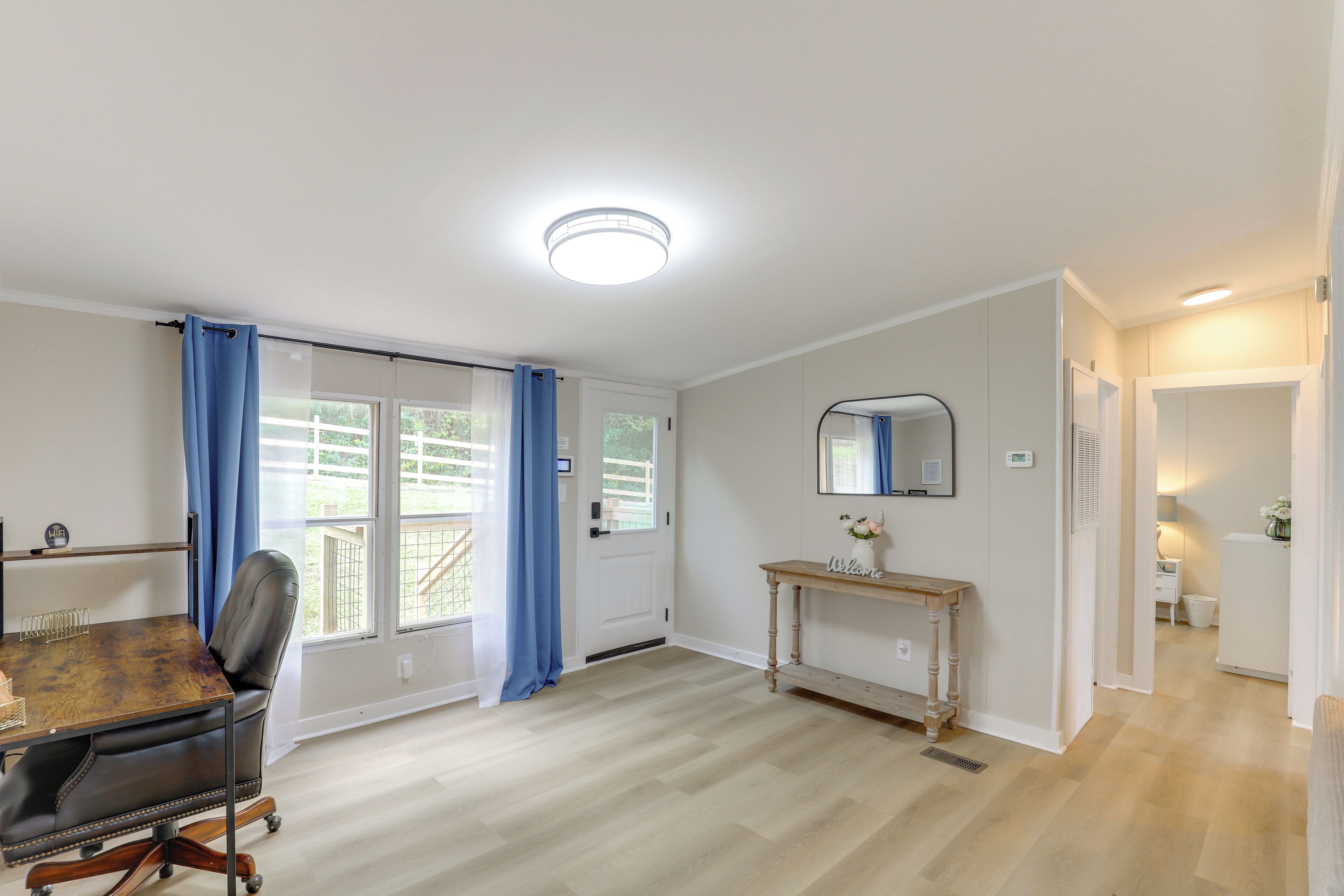 A spacious room with a dining table, a chair, a console table with a mirror, and a view through a door to an outdoor area.