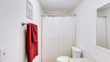 Un bagno con il water bianco, una tenda della doccia, un asciugamano rosso e un quadro appeso al muro.