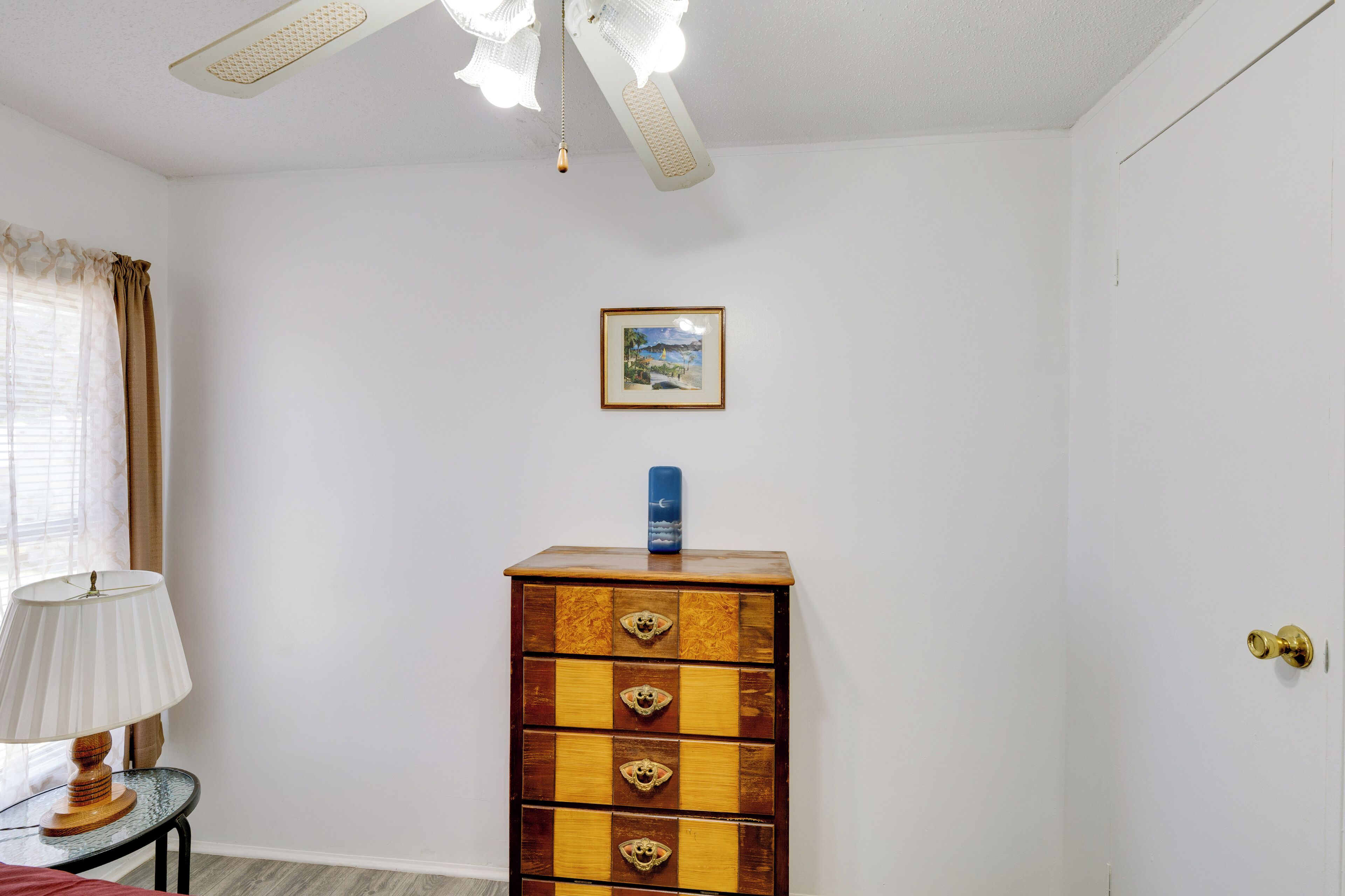 Une pièce avec une commode en bois, un tableau encadré au mur et une lampe sur une table d’appoint.