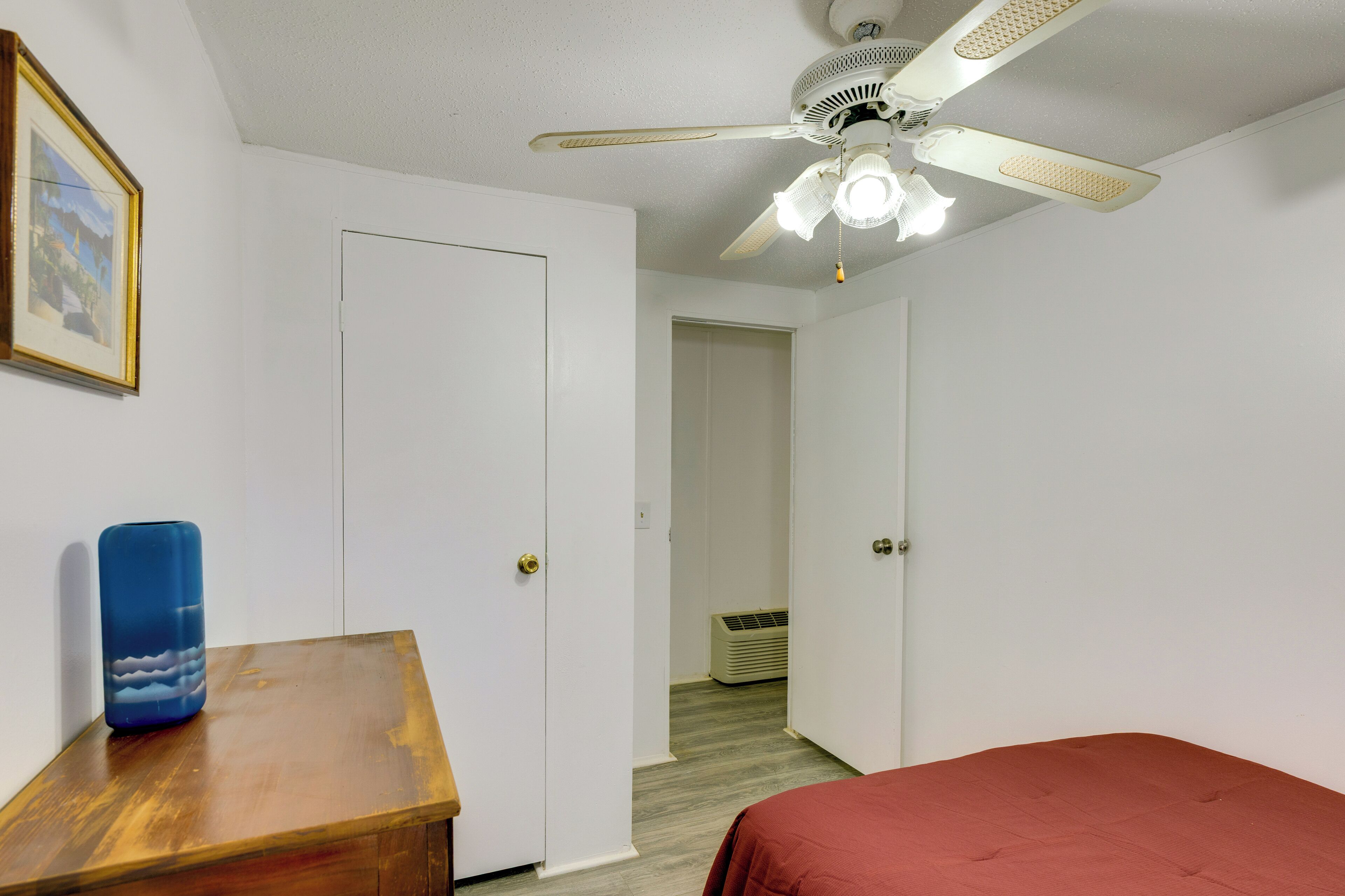 A bedroom with a bed, a wooden nightstand, a ceiling fan, and a framed picture on the wall.