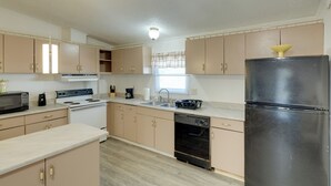 Una cucina con mobili beige, un frigorifero nero, un fornello, un forno a microonde ed una lavastoviglie.