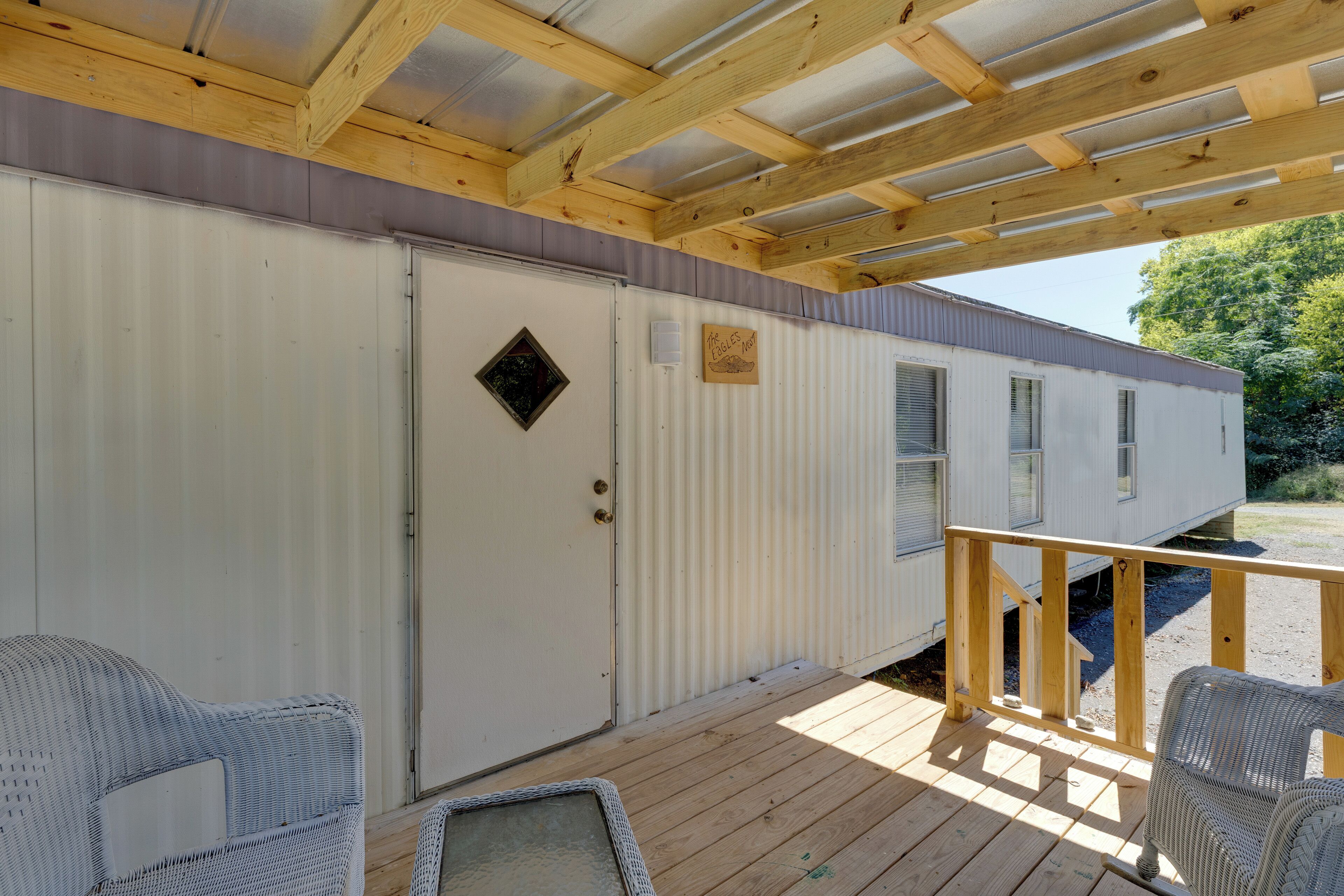 En overdækket veranda med fletstole, en træterrasse og en campingvogn med lukket dør og vinduer.