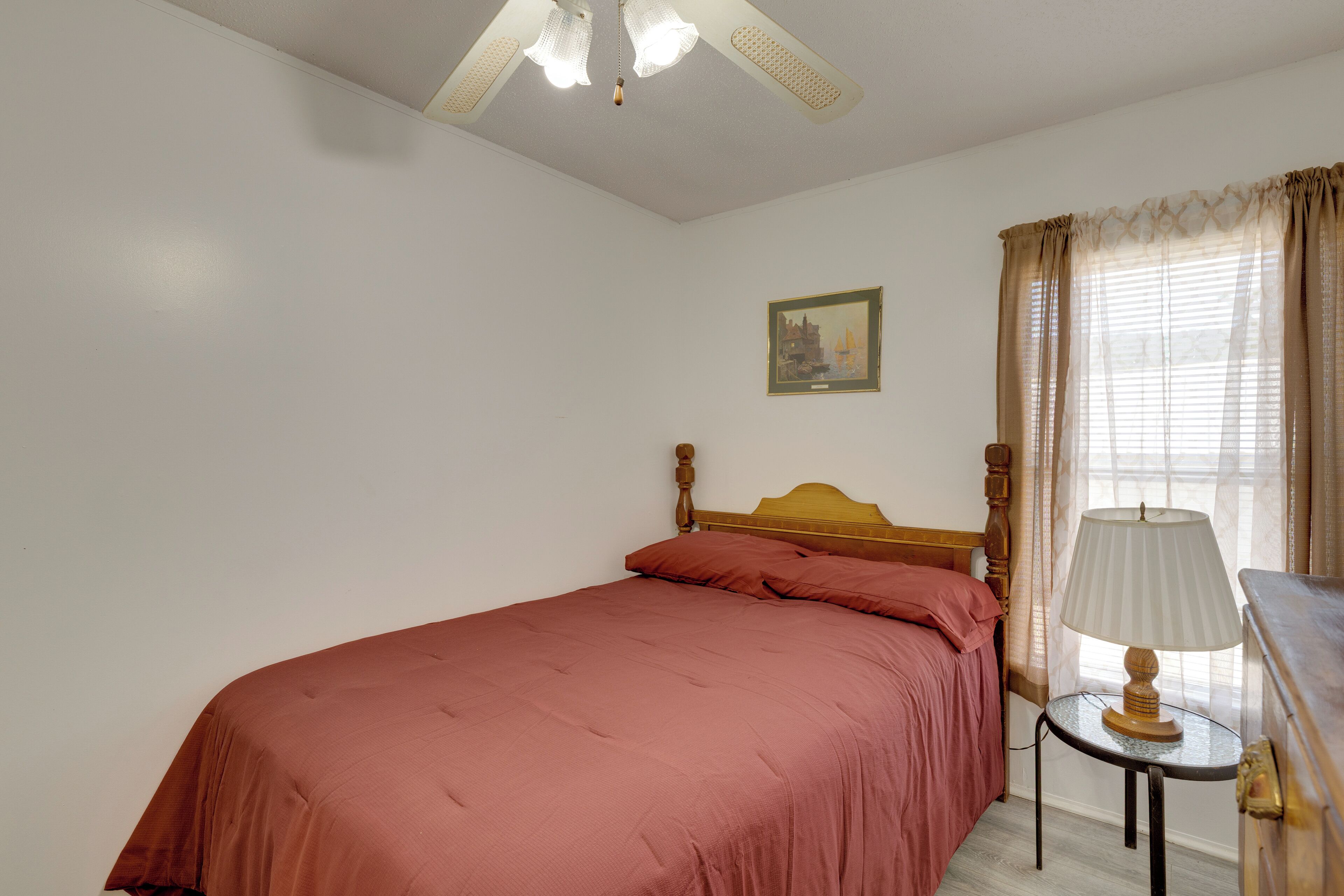 Una cama individual con cabecera de madera, una mesita de noche con lámpara y una ventana con cortinas.