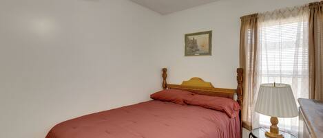 Una cama individual con cabecera de madera, una mesita de noche con lámpara y una ventana con cortinas.