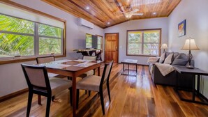 A spacious room with a wooden ceiling, a dining area with a table and chairs, a sofa, and large windows offering a view of greenery. - Nemo's Loft: Panoramic 2BR/2BA Beachfront View in Ambergris Caye (San Pedro)