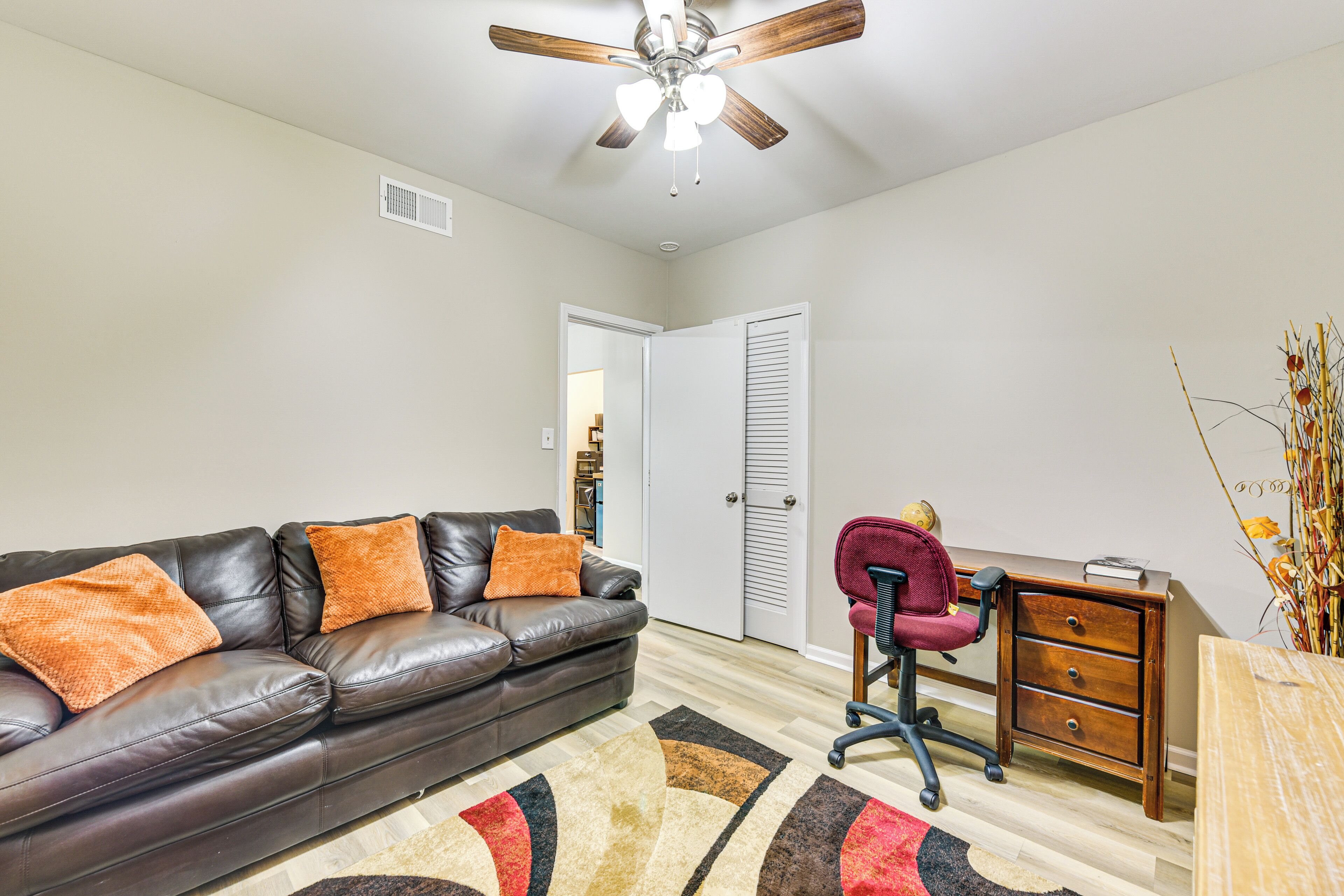A living room with a leather sofa, a wooden desk, and a ceiling fan.