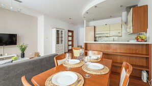 Un coin repas avec une table en bois dressée pour quatre personnes, un téléviseur et une cuisine en arrière-plan.