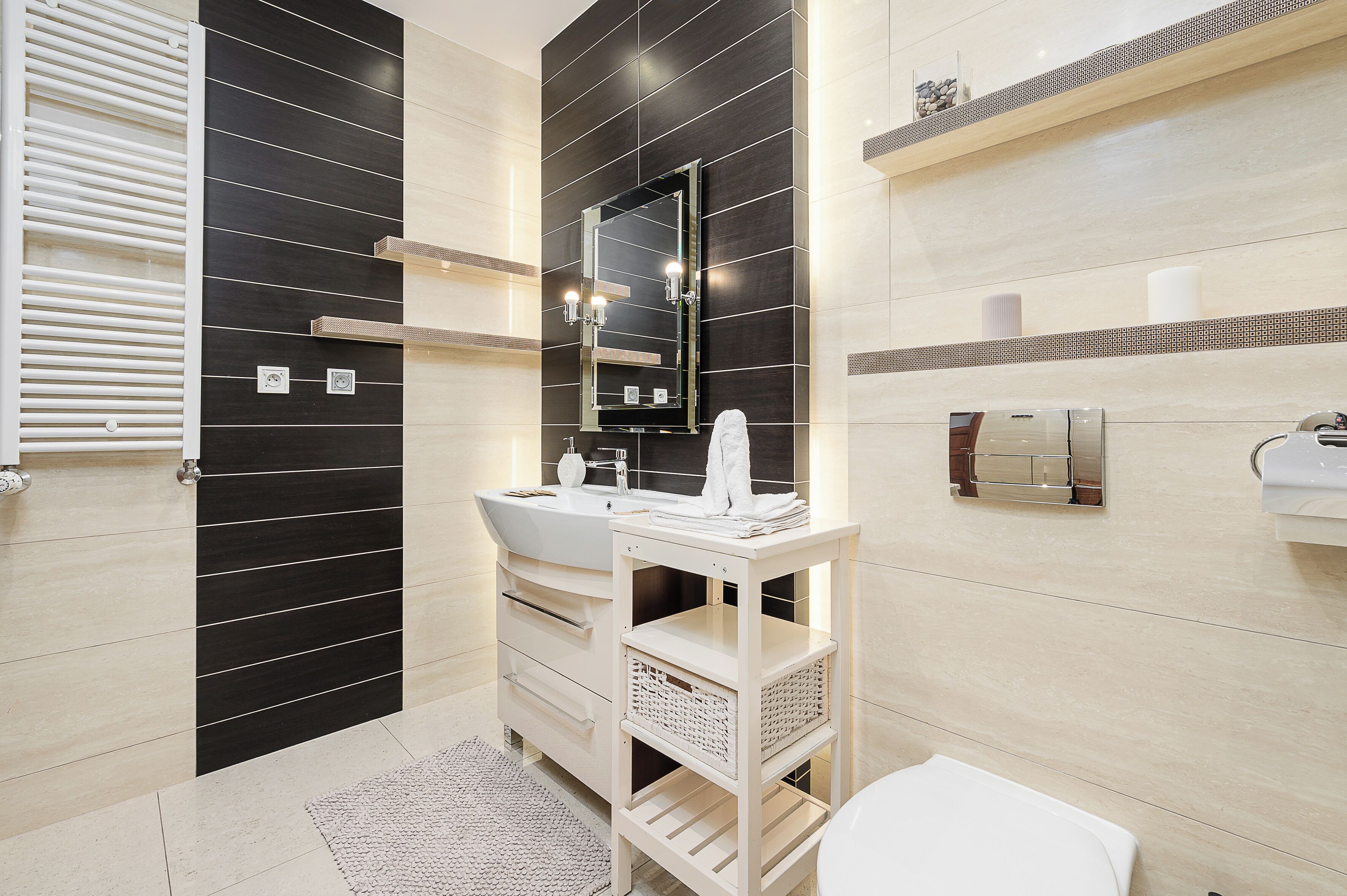 A modern bathroom with a black and white tiled wall, a white sink, a mirror, and a towel rack.