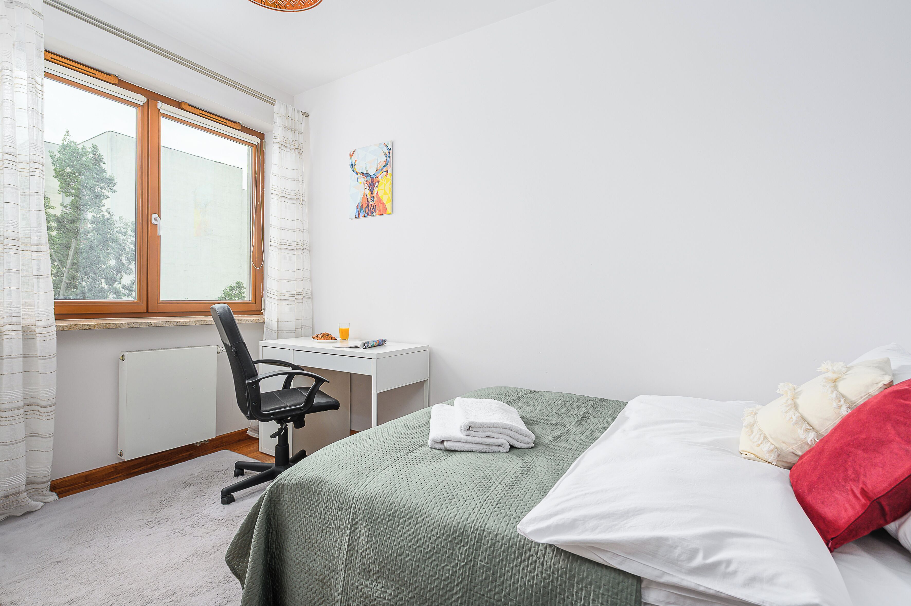 A bedroom with a bed, a desk, a chair, and a window.