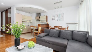 Un salon moderne avec un canapé gris, un coin repas comprenant une table et des chaises, et une cuisine en arrière-plan.