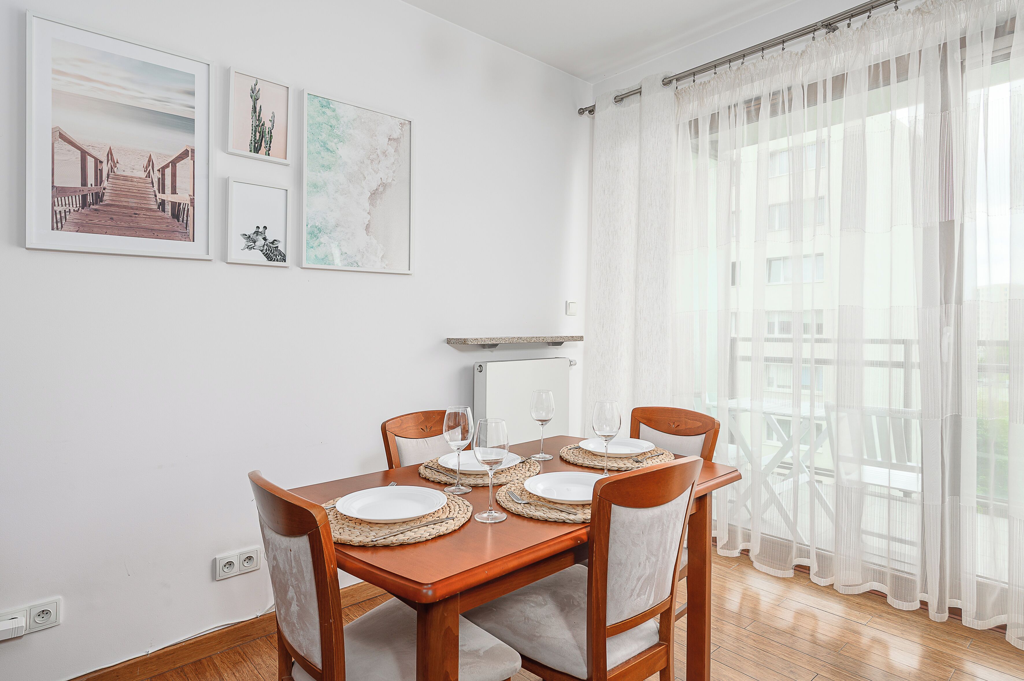 A dining area with a wooden table set for four, white plates, and clear glassware.