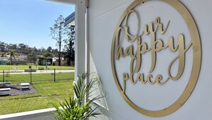 Skilt med teksten 'happy place' på en bygning, med udsigt til en park og et hegn.
