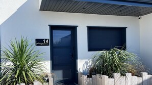 Een modern gebouw met een donkerblauwe deur, een klein raam en een bord waarop het adres 14 staat.
