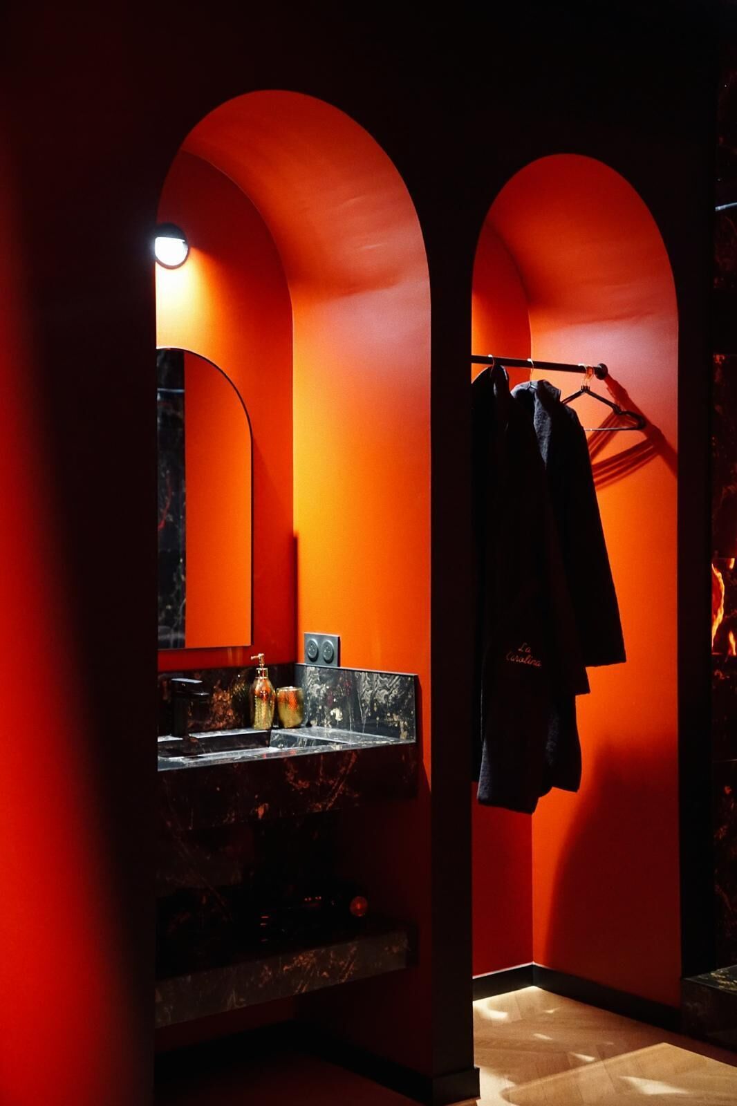 Une salle de bain aux couleurs rouge et noir, comprenant un miroir, un lavabo avec un plan de toilette en marbre et un porte-serviettes sur lequel est suspendue une serviette.