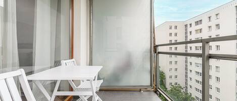 A balcony with a white table and chairs, a sliding glass door, and a view of adjacent buildings.