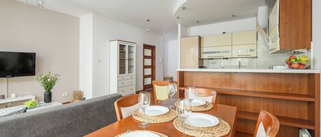 A dining area with a wooden table set for four, a television, and a kitchen in the background.