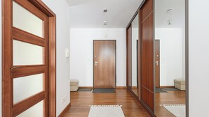A hallway with wooden flooring, a central door, and a mirror on the right. - P&O Apartments KEN (Warsaw)
