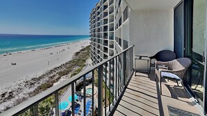 Un balcón con vista a una playa, un área de piscina y un edificio de diseño moderno.