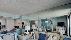 Una sala de estar moderna con un amplio sofá modular, un comedor y una cocina visibles a través de un separador de vidrio.