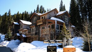 A large, multi-story lodge with a wooden exterior and multiple balconies, surrounded by snow and trees.