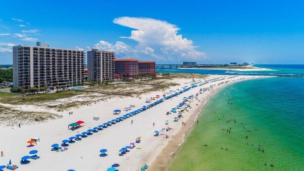Een strandresort met meerdere hoge gebouwen, een uitgestrekt strand met parasols en helderblauw water.