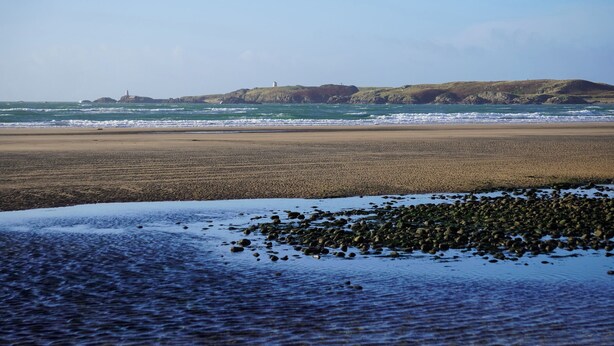Une plage avec un rivage rocheux et un phare visible au loin.