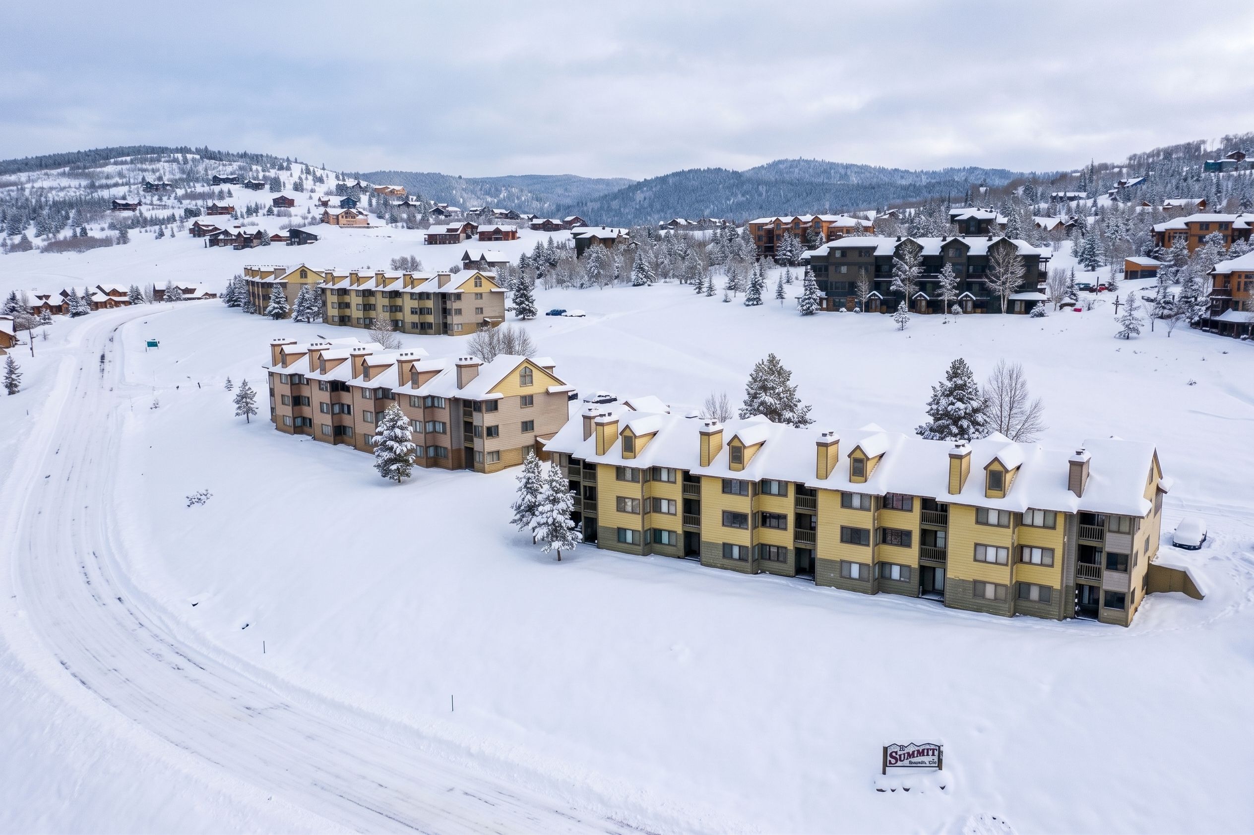Une station de ski enneigée, dotée de plusieurs bâtiments d’hébergement, dont un imposant bâtiment jaune sur lequel on peut lire l’inscription « Summit ».