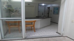 Una cocina con encimera blanca, dos sillas de madera y un vidrio que da a otra habitación.