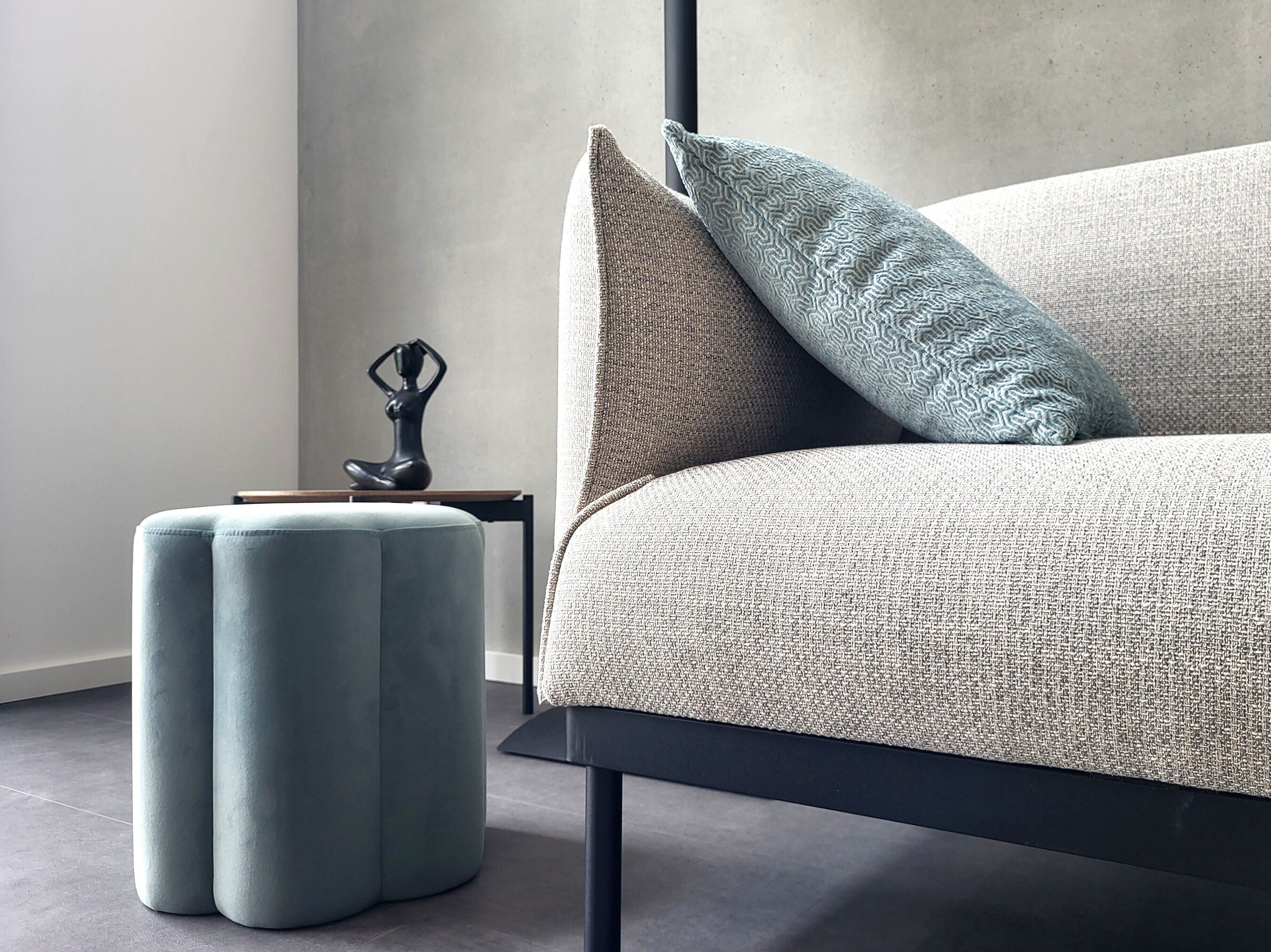 Ein modernes Zimmer mit einer Couch, einem gemusterten Zierkissen, einem kleinen Tisch mit einer Skulptur und einem passenden Hocker.