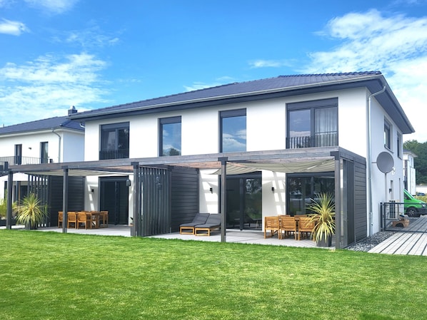 Une maison moderne à deux étages, dotée d’un patio couvert, de grandes fenêtres et d’une pelouse bien entretenue.