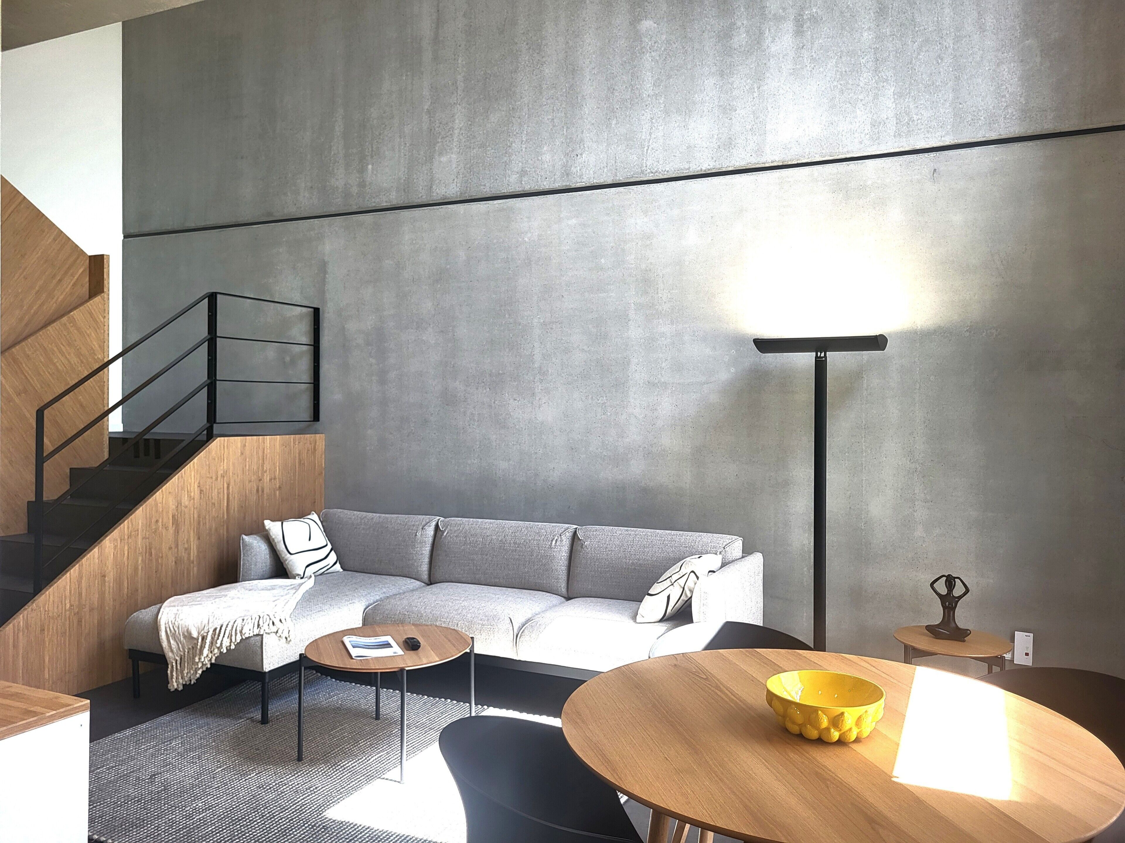 A modern living room with a grey sofa, a wooden coffee table, a round table with a yellow bowl, a floor lamp, and a staircase.