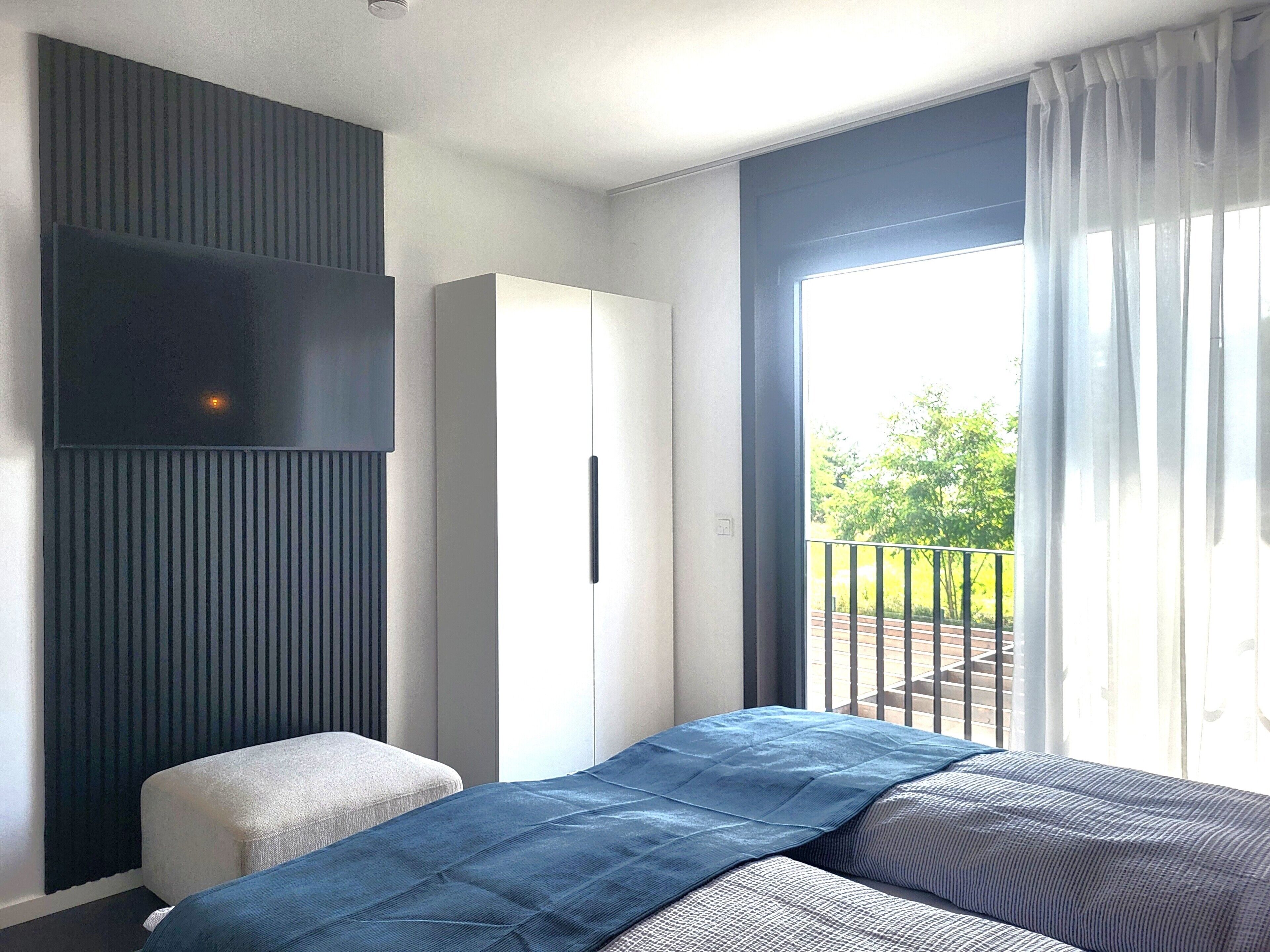A bedroom with a bed, a wardrobe, a bench, and a balcony with a railing.