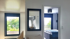 Une chambre avec un lit, une chaise, un grand miroir et une vue sur un balcon.