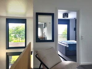 A room with a bed, a chair, a large mirror, and a view of a balcony.
