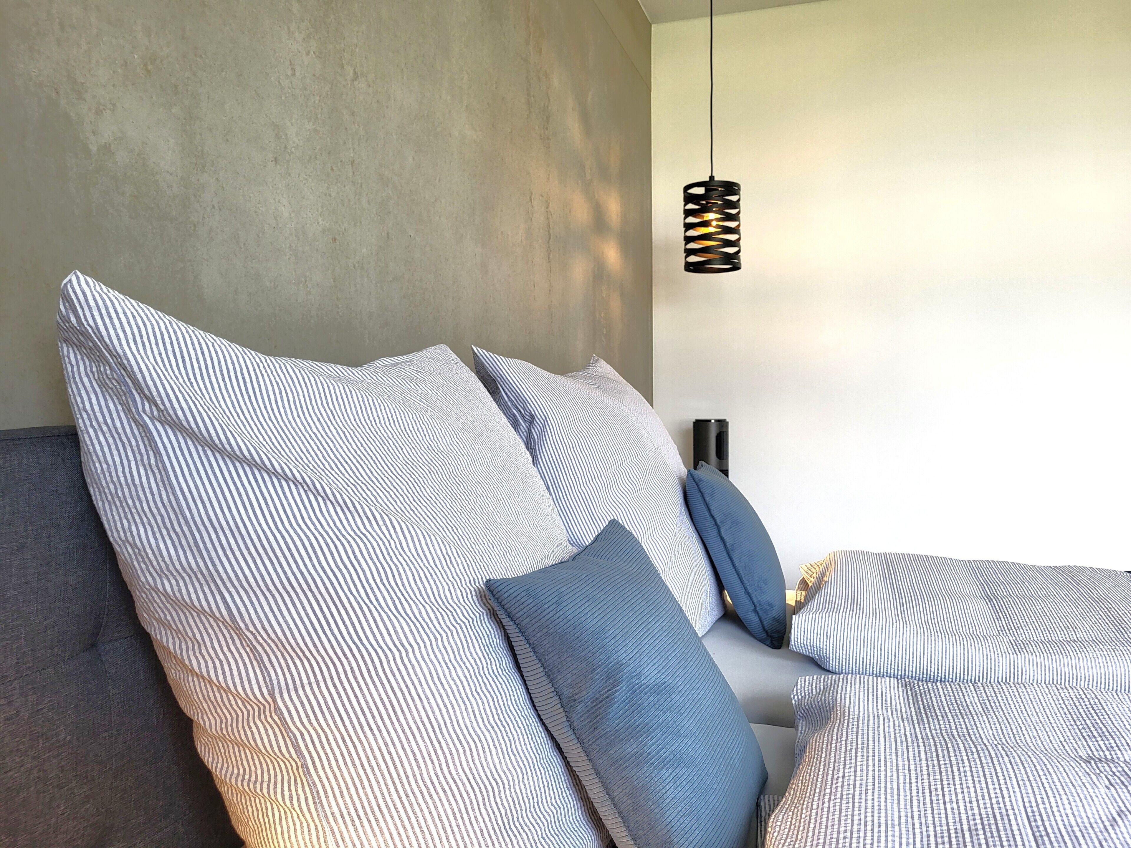 Een bed met gestreept beddengoed en een hanglamp.